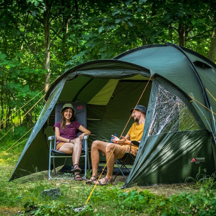 Load image into Gallery viewer, Two people sitting outside a green tent in a forest