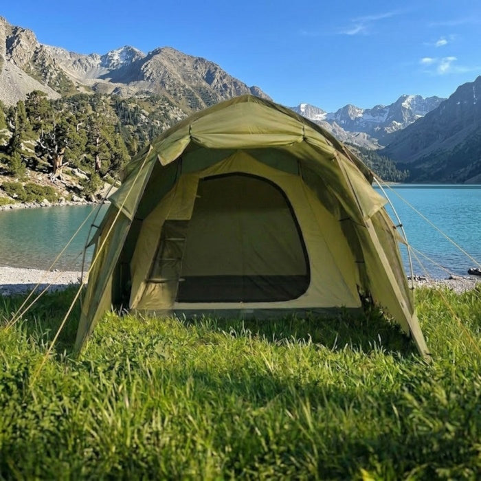 Load image into Gallery viewer, khaki tent set up in a grassy area with trees and mountains in the background