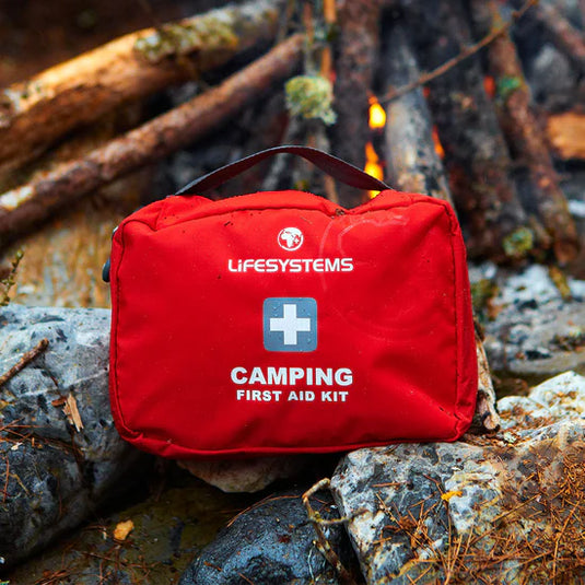 Red Lifesystems camping first aid kit on a rocky surface with a campfire in the background
