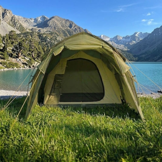 khaki tent set up in a grassy area with trees and mountains in the background